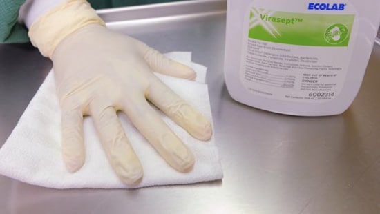 EVS worker in OR using non-linting cloth and Virasept to clean Mayo Tray